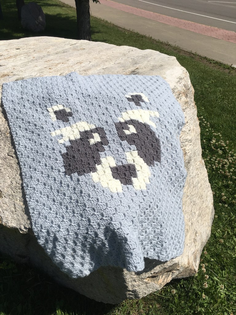 The Bandit stroller blanket is draped on a very large rock.