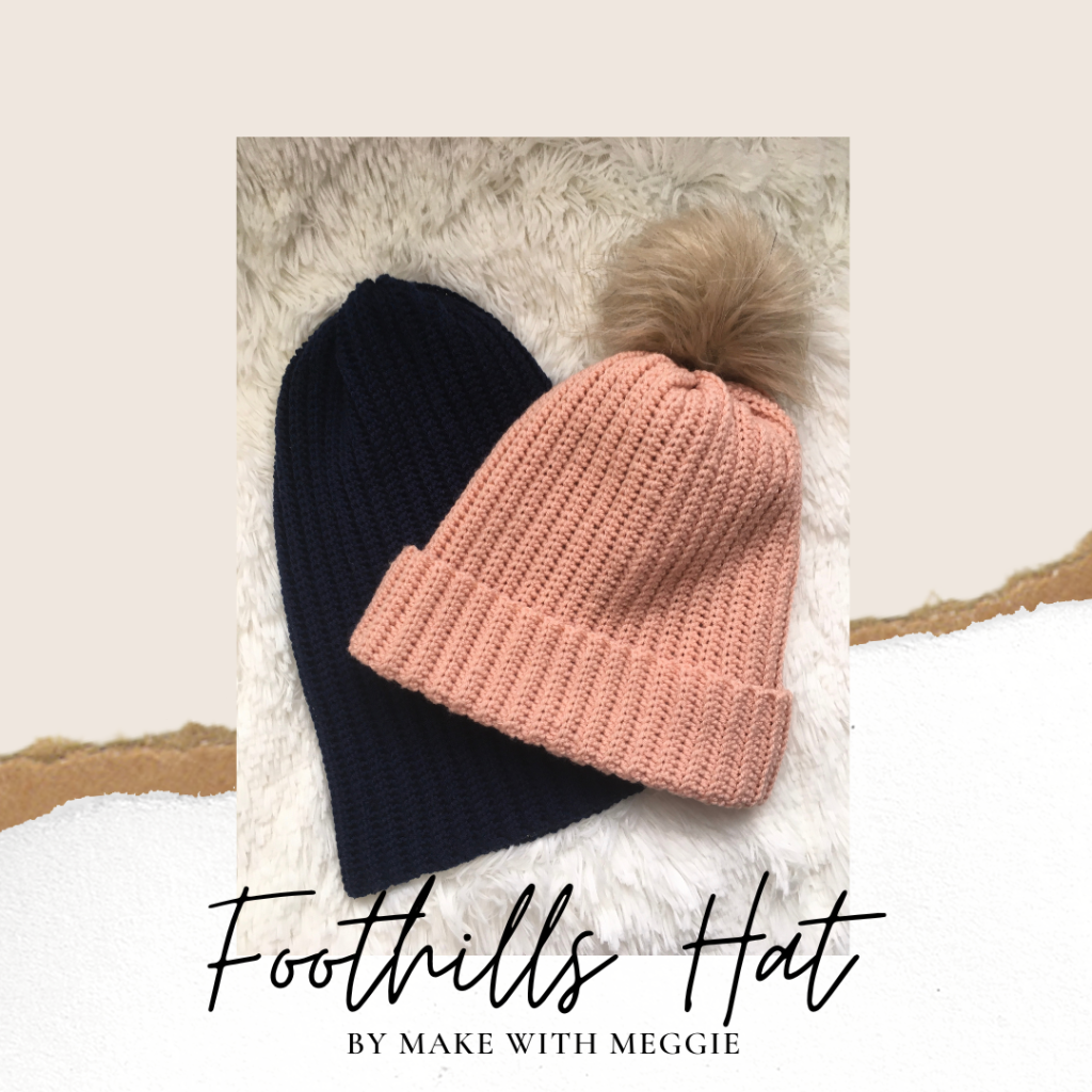 Two of the Foothills Hat, one in pink with a folded brim and taupe faux fur pom-pom and one in navy blue rest together on a white faux fur background. the picture is on background of taupe with exposed an exposed edge of each cardboard and white paper visible at a small angle across the middle. Near the bottom black text reads foothills hat by make with meggie.